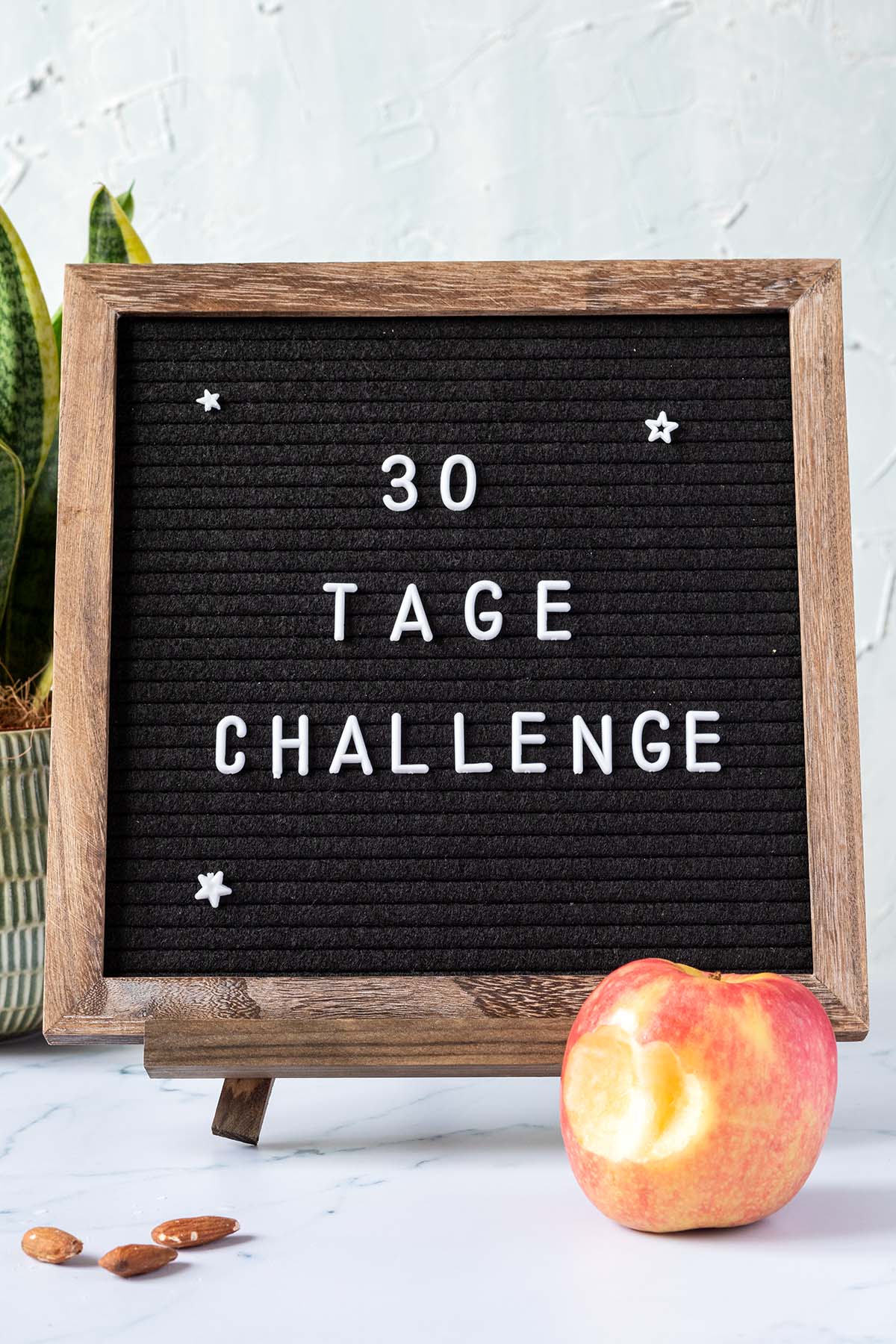 Eine Buchstabentafel mit dem Schriftzug "30 Tage Challenge" vor einem wei&szlig;en Hintergrund und einem angebissenen Apfel davor.
