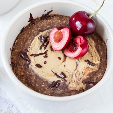 Schoko Baked Oatmeal mit Cashewmus, geschmolzener Schokolade und zwei frischen Kirschen