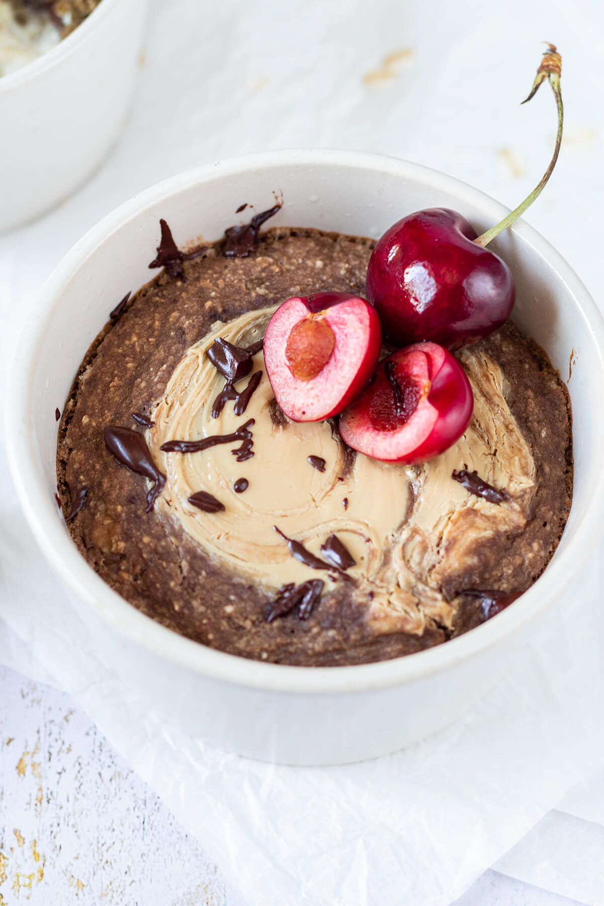 Schoko Baked Oatmeal mit Cashewmus, geschmolzener Schokolade und zwei frischen Kirschen