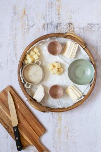 Holzbrett mit kleinen leeren Sch&uuml;sseln und in Scheiben und W&uuml;rfel geschnittenem K&auml;se drauf. Daneben ein leeres Schneidebrett