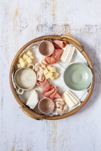 Brotzeitplatte mit vier kleinen, leeren Sch&uuml;sseln, K&auml;sew&uuml;rfeln und Schinken.