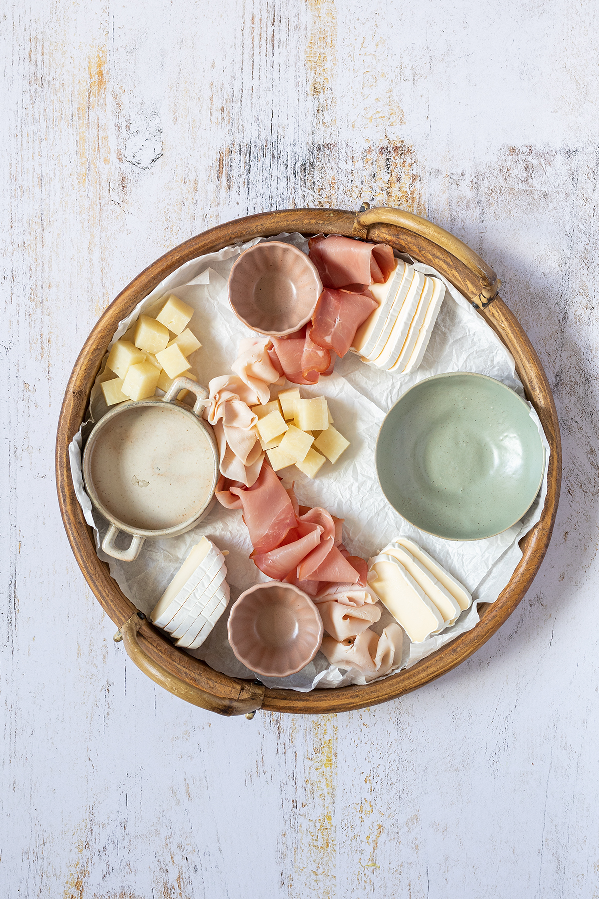 Brotzeitplatte mit vier kleinen, leeren Sch&uuml;sseln, K&auml;sew&uuml;rfeln und Schinken.