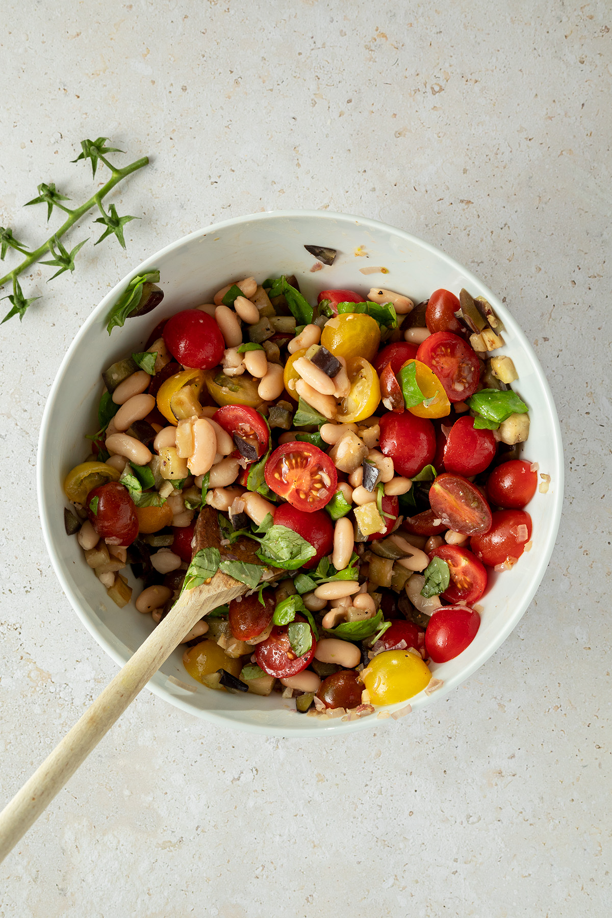 Cannellini Bohnen, Tomaten, Auberginen und Basilikumbl&auml;tter werden in einer gro&szlig;en Salatsch&uuml;ssel mit einem Kochl&ouml;ffel umger&uuml;hrt