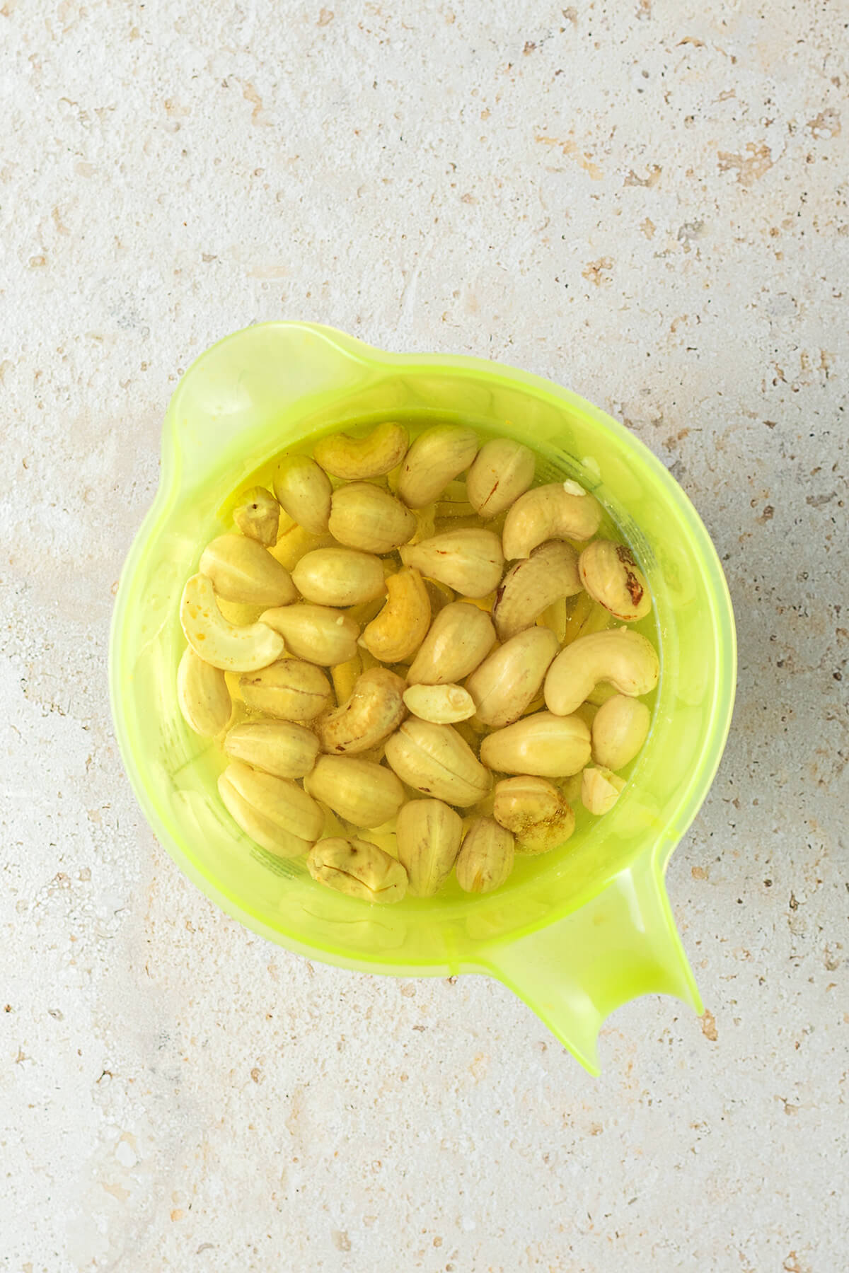 In Wasser eingeweichte Cashewn&uuml;sse in einem gr&uuml;nen Messbecher.