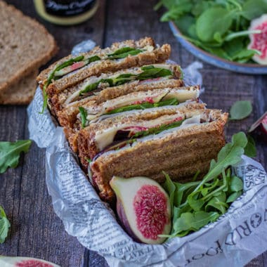Mehrere Sandwiches mit K&auml;se und Feigen in einer Brotzeitbox mit frischen Feigen und Deko im Bildrand.