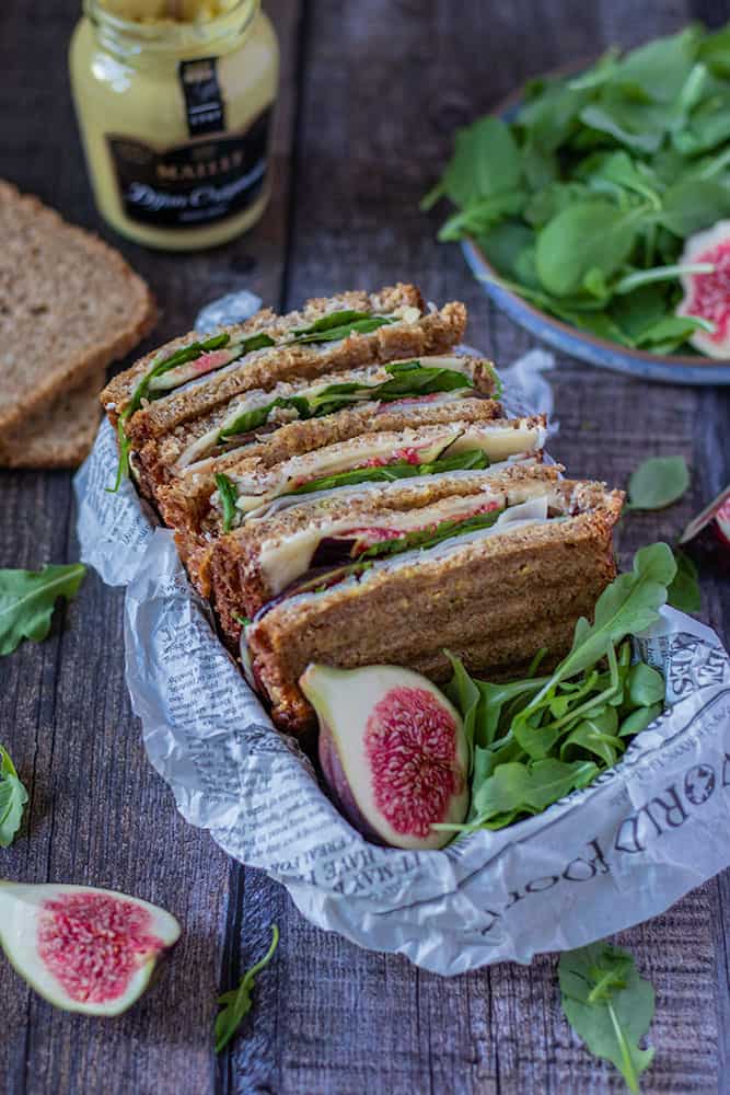 Mehrere Sandwiches mit K&auml;se und Feigen in einer Brotzeitbox mit frischen Feigen und Deko im Bildrand.