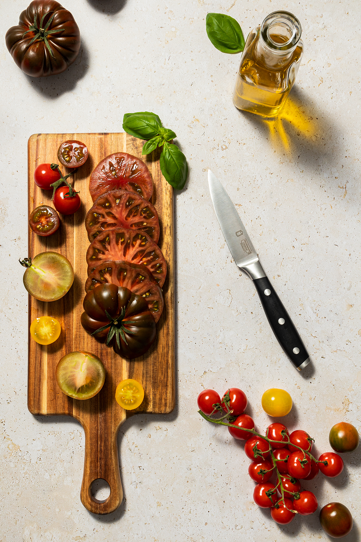 Rezeptserie zum Thema Sommerrezepte mit Tomaten - bunte Tomaten auf einem Schneidebrett, Oliven&ouml;l im Hintergrund