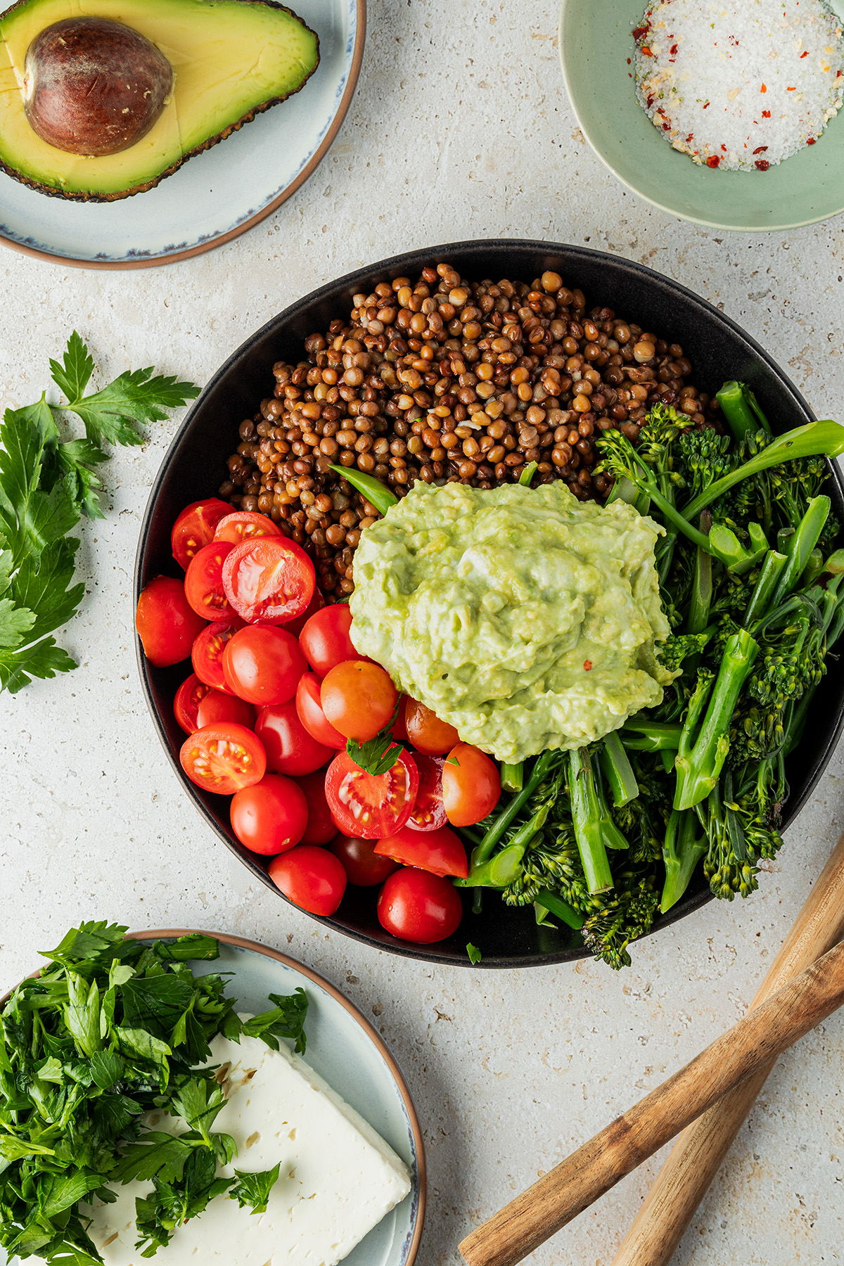 Zutaten für den Linsensalat in einer flachen Schüssel: Brokkoli, Tomaten, Linsen und Guacamole