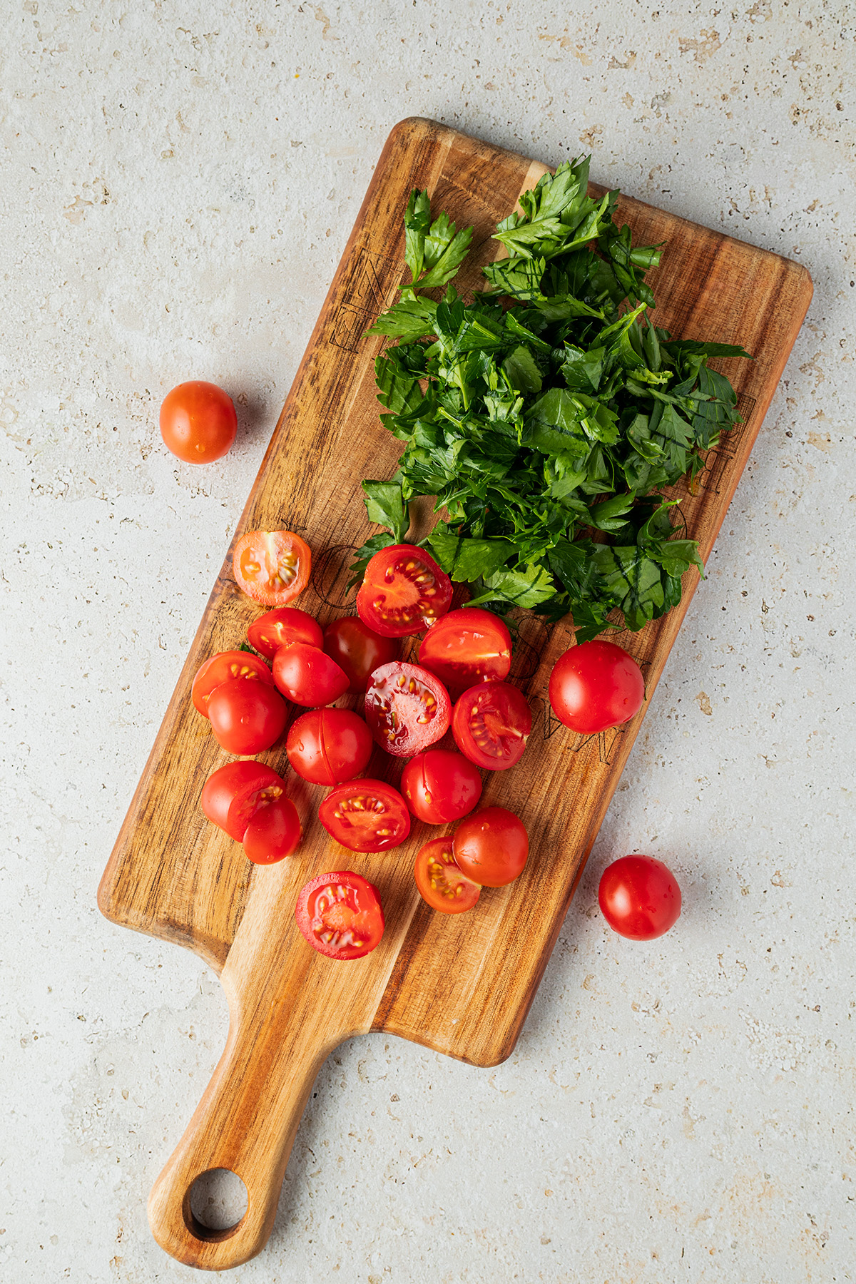 halbierte Cherry Tomaten und grob gehackte Petersilie auf einem Brett