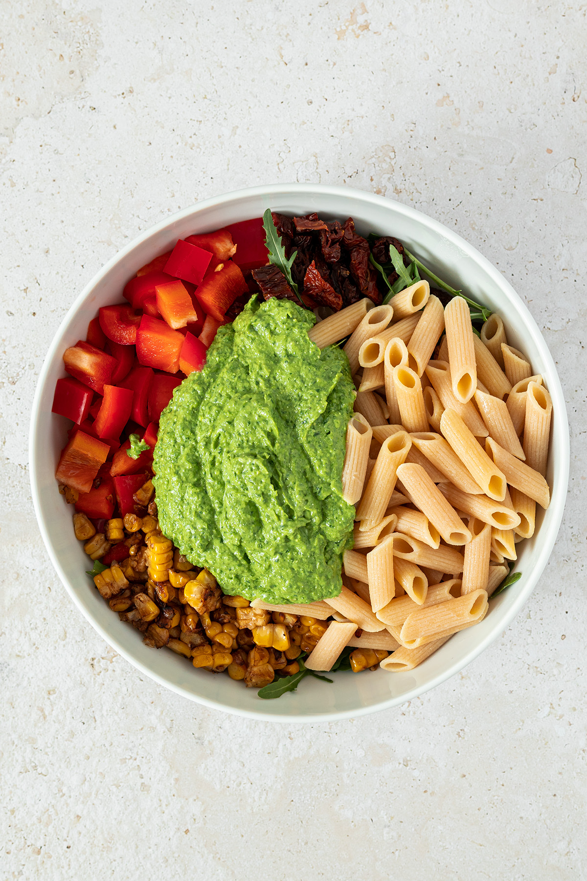gekochte Nudeln, Salat, getrocknete Tomaten, Paprika, ger&ouml;steter Mais und gr&uuml;ne Pesto in einer gro&szlig;en Sch&uuml;ssel