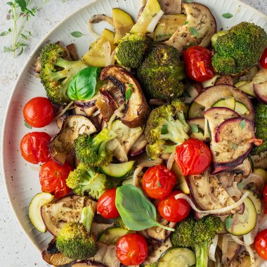 Buntes Ofengem&uuml;se vom Blech mit Tomaten, Brokkoli, Aubergine und Zucchini serviert auf einem gro&szlig;en, wei&szlig;en Teller.