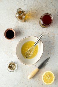 Zubereitung der Marinade: Eine kleine Sch&uuml;ssel mit Zitronensaft und fein gew&uuml;rfeltem Knoblauch, daneben eine Sch&uuml;ssel mit getrockneten Kr&auml;utern und Salz, Balsamico, Honig und eine Flache Oliven&ouml;l