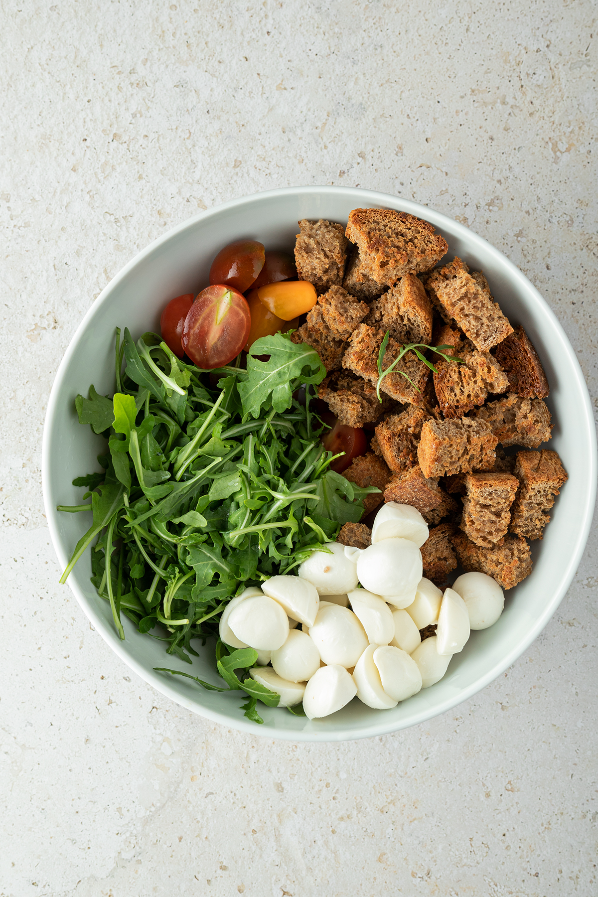 ger&ouml;stete Brotw&uuml;rfel, Mozzarella, Rucola und halbierte Cherrytomaten in einer Salatsch&uuml;ssel