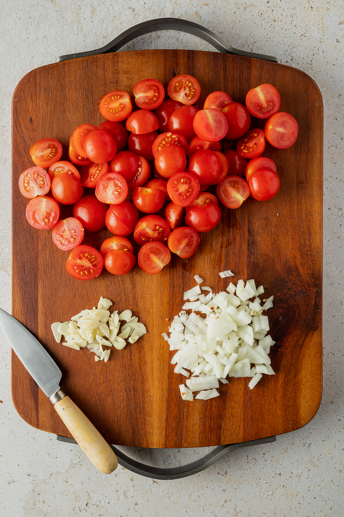 halbierte Cherrytomaten, fein gew&uuml;rfelte Schalotte und feine Knoblauchscheiben auf einem Holzbrett