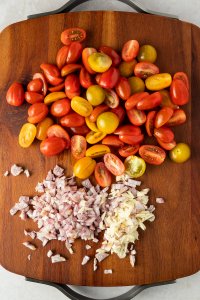 halbierte Tomaten, fein gewürfelter Knoblauch und Schalotte auf einem Schneidebrett