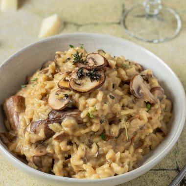 Teller mit cremigen Steinpilzrisotto auf grünen Fließen, Parmesan und ein Weinglas im Hintergrund.