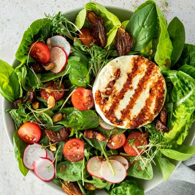 Salat Bowl mit Grillk&auml;se, Cherrytomaten, Datteln, d&uuml;nnen Radieschen Scheiben und N&uuml;ssen.
