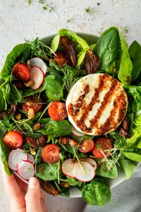 Salat Bowl mit Grillk&auml;se, Cherrytomaten, Datteln, d&uuml;nnen Radieschen Scheiben und N&uuml;ssen.