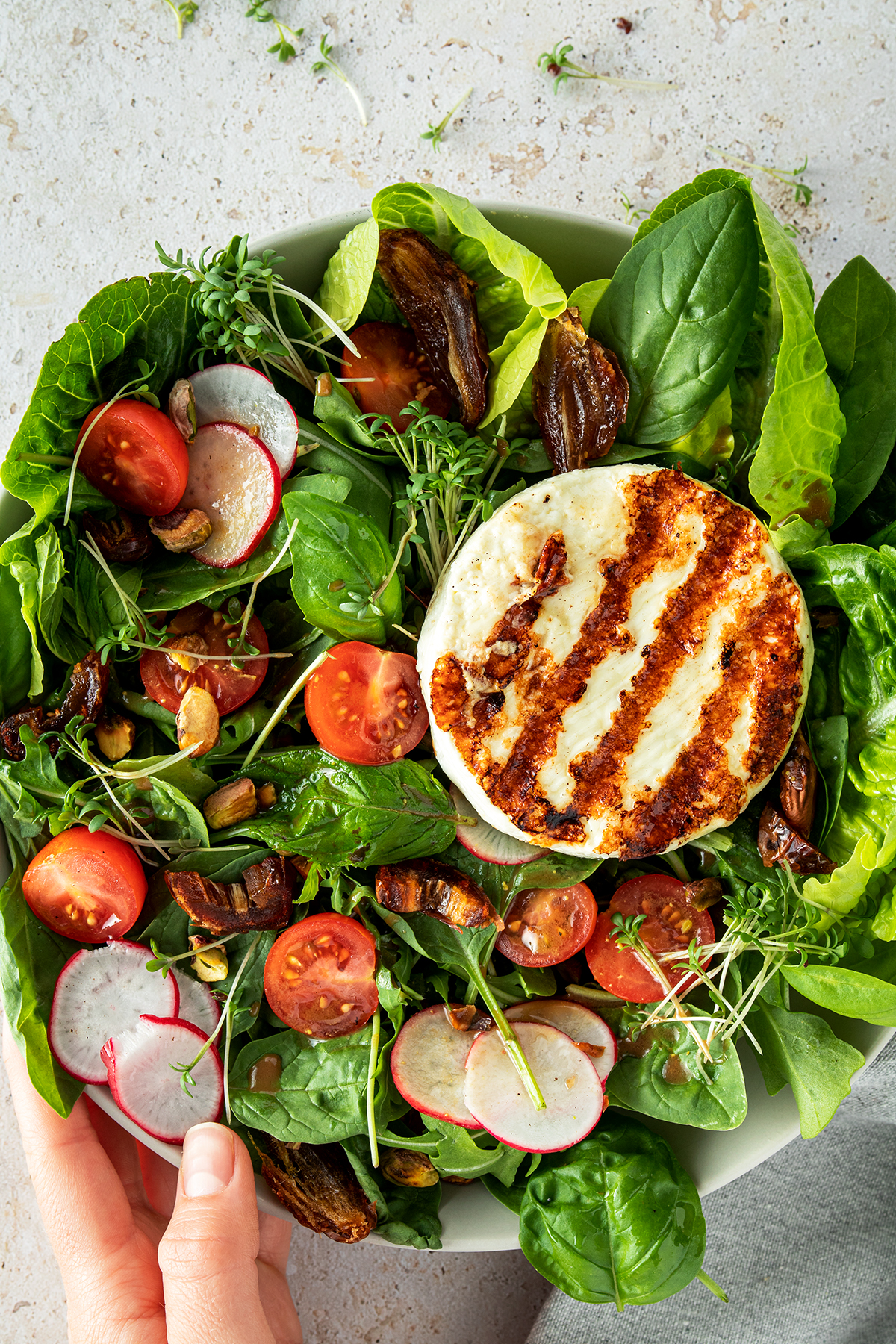 Salat Bowl mit Grillk&auml;se, Cherrytomaten, Datteln, d&uuml;nnen Radieschen Scheiben und N&uuml;ssen.