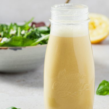Salatdressing in einer Glasflasche, im Hintergrund eine Salatsch&uuml;ssel und eine halbe Zitrone