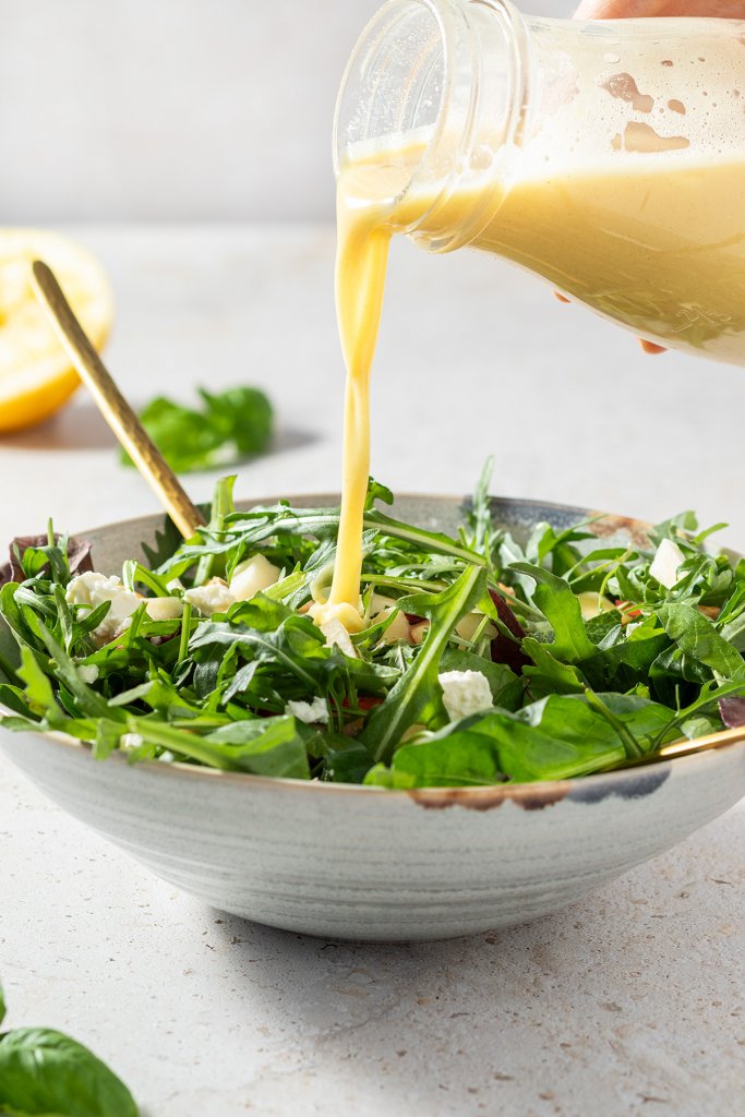 Salatdressing wird auf einen Sch&uuml;ssel mit Salat gegossen