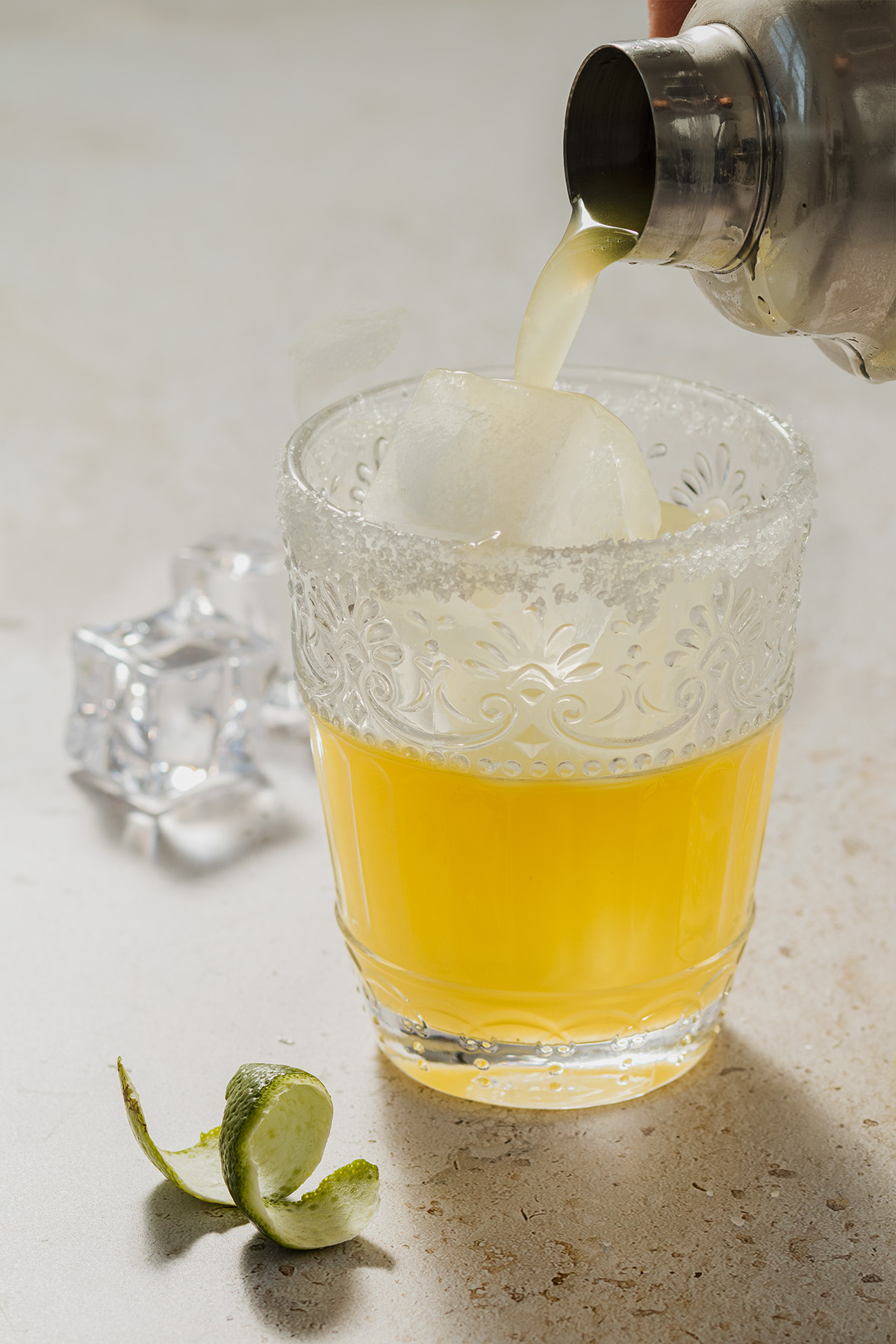 Der Skinny Margarita Cocktail wird aus dem Cocktail Shaker in ein Glas mit Eisw&uuml;rfel und Salzrand eingegossen