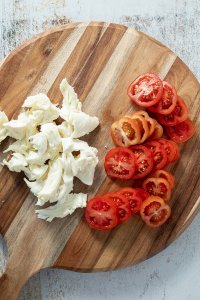 Tomatenscheiben und Mozzarella-St&uuml;ckchen auf einem Holzbrett.