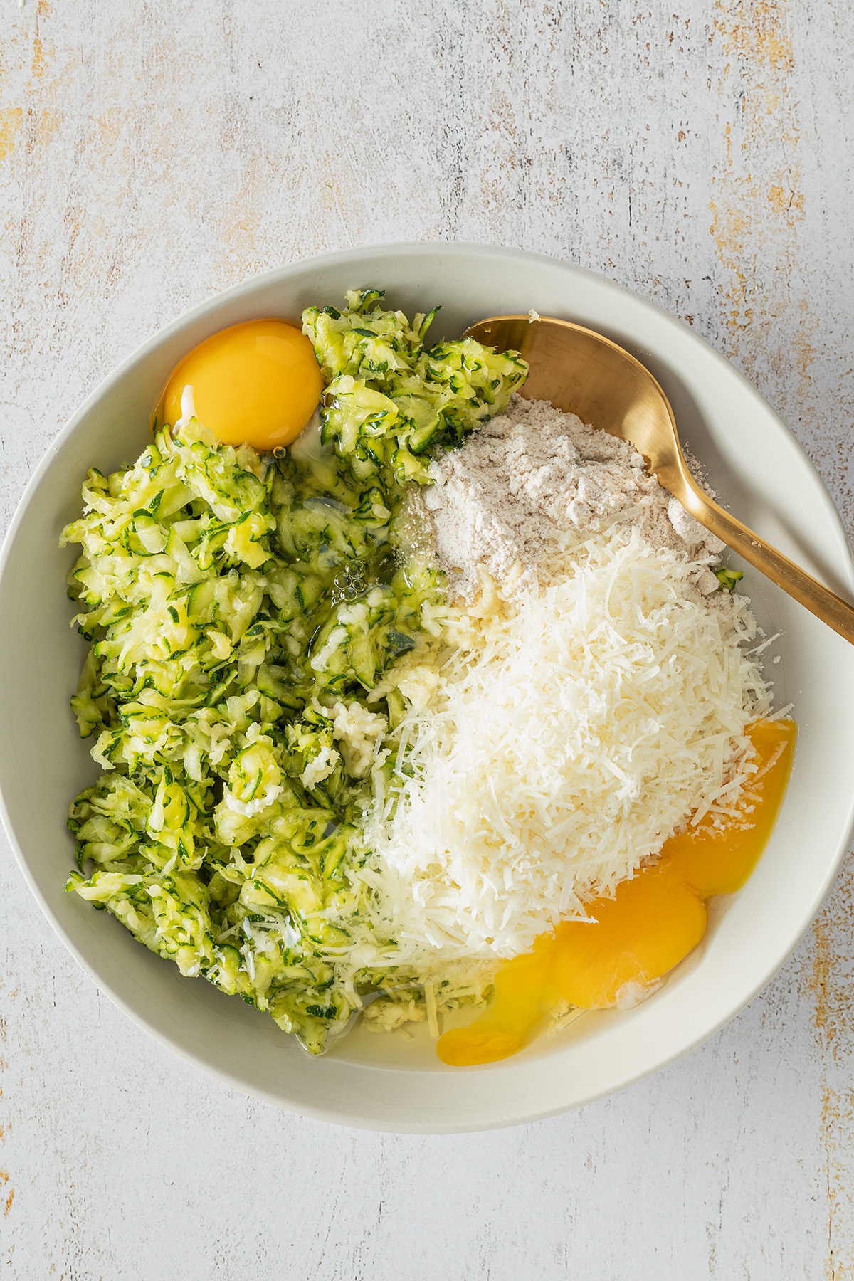 Zucchiniraspeln, zwei Eier, Mehl und geriebener K&auml;se in einer Sch&uuml;ssel.
