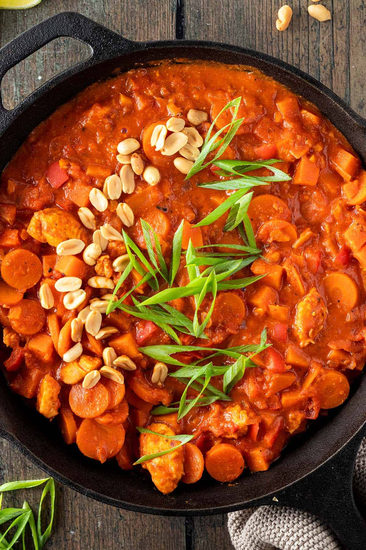 Afrikanischer Erdnusseintopf in einer massiven Pfanne, serviert mit frischen Fr&uuml;hlingszwieblen und Erdn&uuml;ssen als Deko.