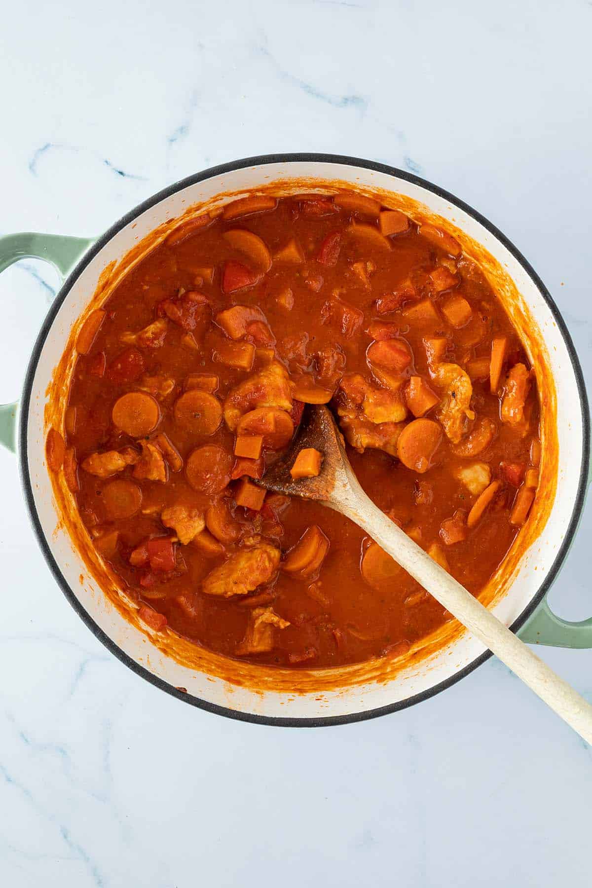 Fertiger Erdnusseintopf mit Gem&uuml;se und einer cremigen Tomaten-Erdnusssauce in einem Topf mit einem Kochl&ouml;ffel.