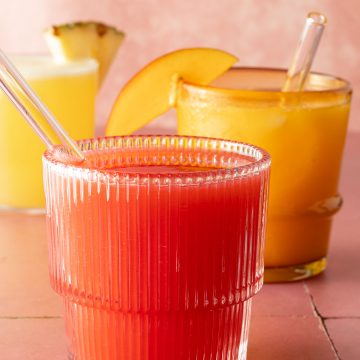 Drei Gl&auml;ser Agua Fresca in verschiedenen Farben, vorne rote Erdbeer Agua Fresca mit Glasstrohhalm.