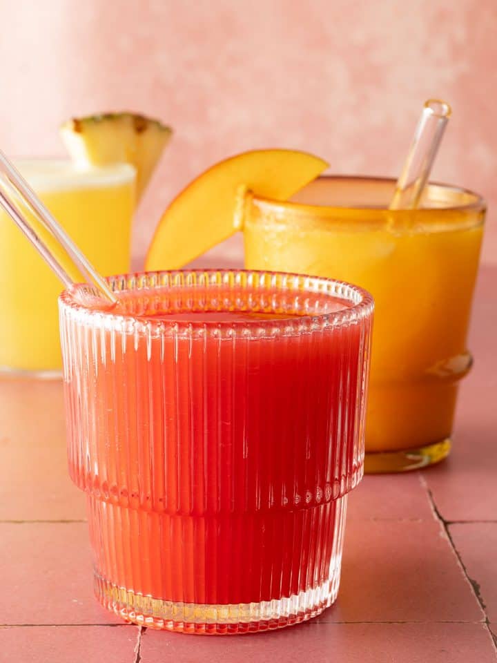 Drei Gl&auml;ser Agua Fresca in verschiedenen Farben, vorne rote Erdbeer Agua Fresca mit Glasstrohhalm.