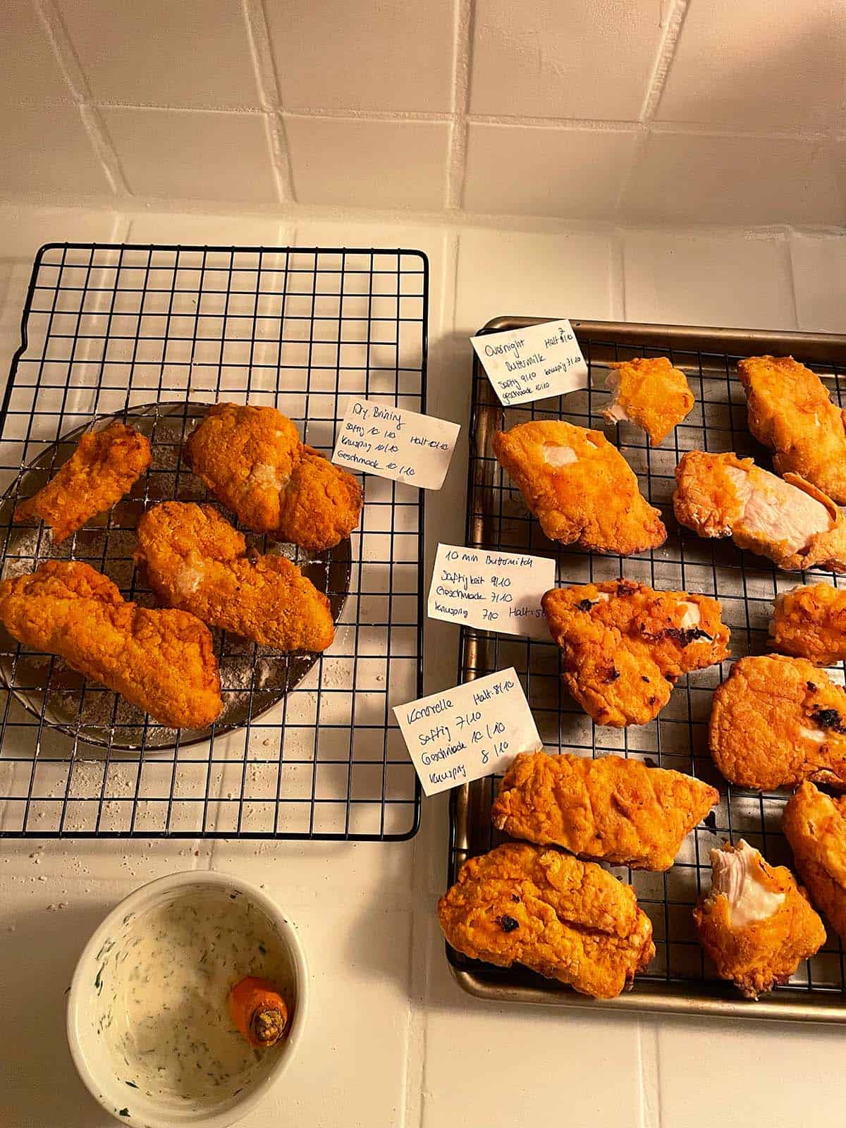 4 verschiedene Testversuche von Fried Chicken im Airfryer auf einer K&uuml;chenarbeitsfl&auml;che mit jeweiligen Beschriftungskarten. 
