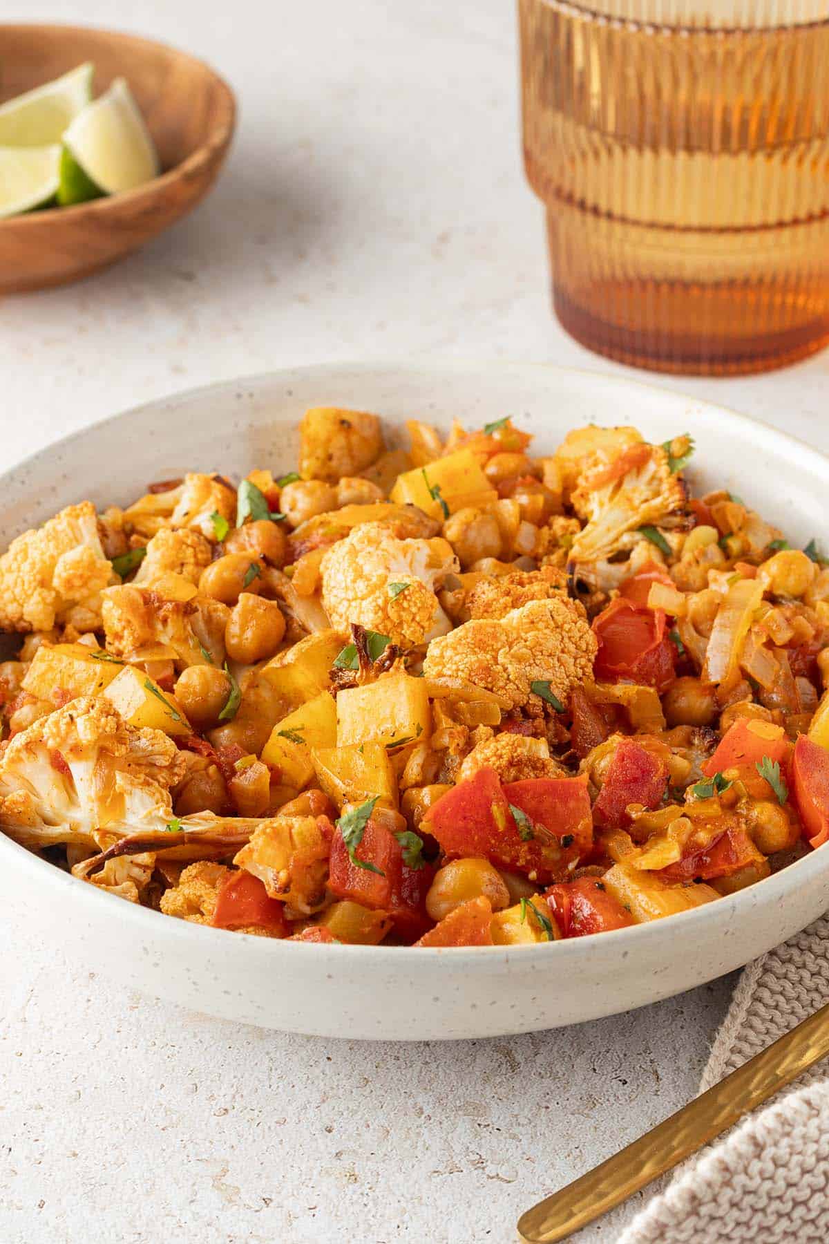 Blumenkohl Kartoffel Curry mit Kichererbsen in einem Teller, Deko im Hintergrund.