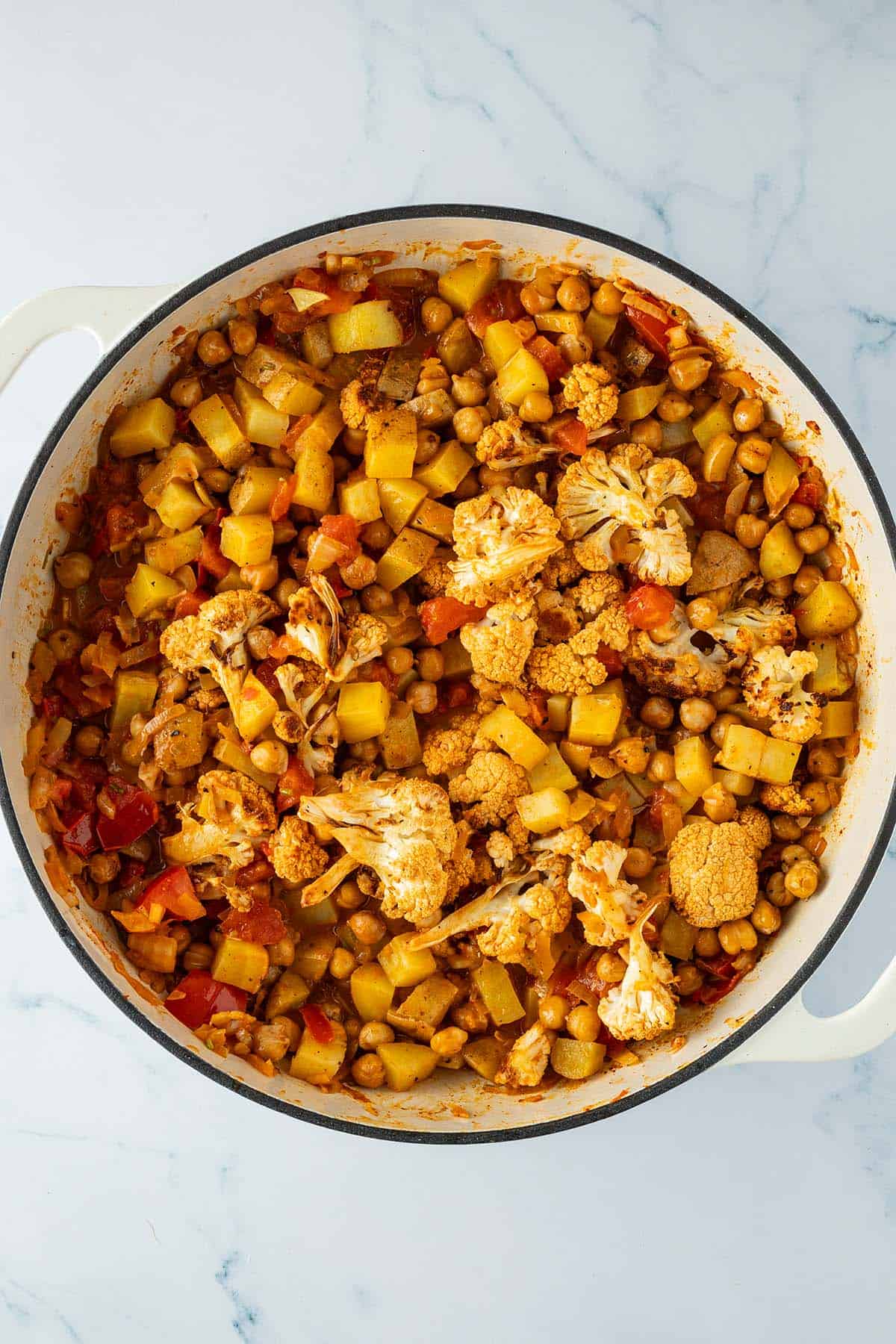 Aloo Gobi in einer gro&szlig;en Gusseisenpfanne mit Kichererbsen.