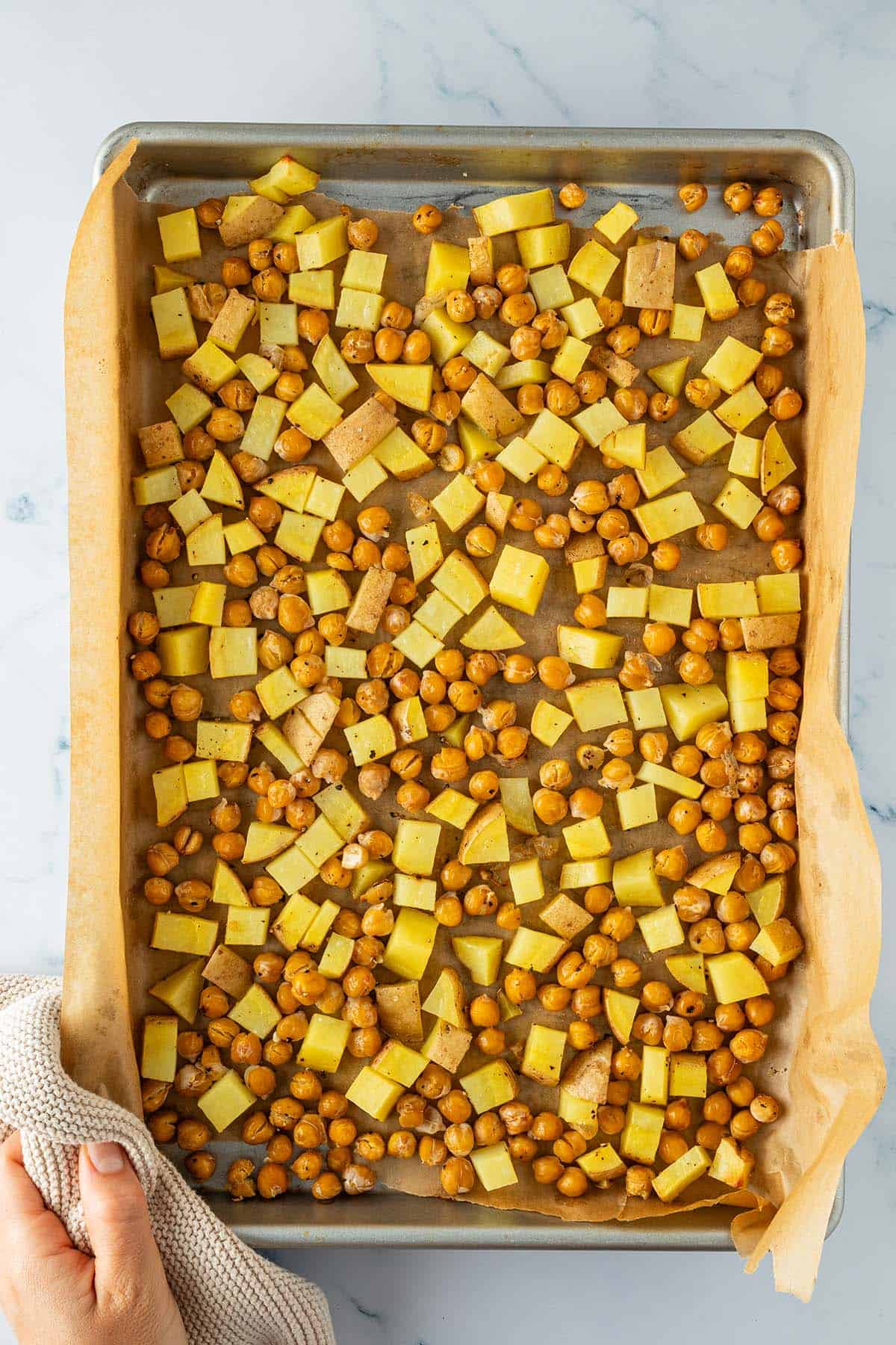 Ger&ouml;stete Kichererbsen und Kartoffel-St&uuml;ckchen auf einem Blech mit Backpapier.