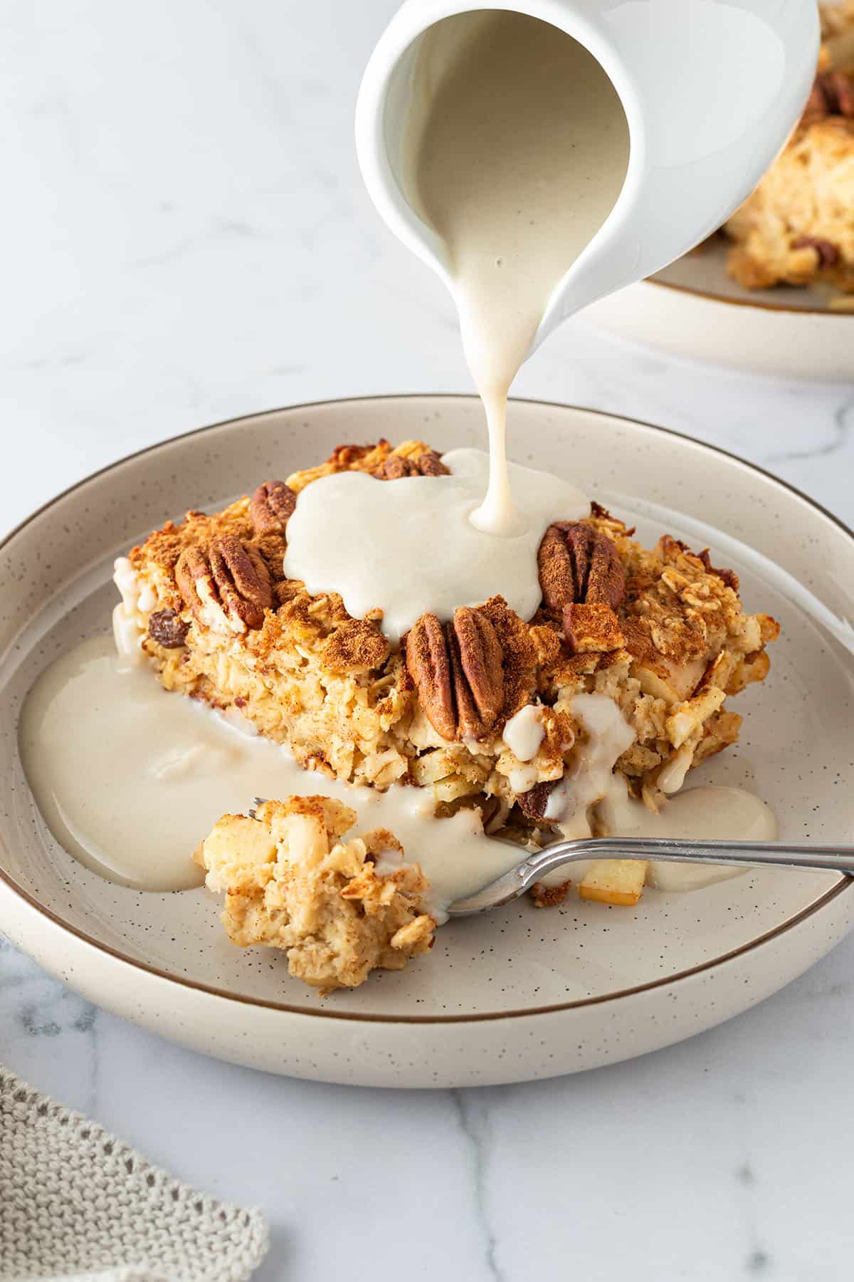 Auf ein St&uuml;ck Apfel Baked Oatmeal wird Vanillesauce gegossen.