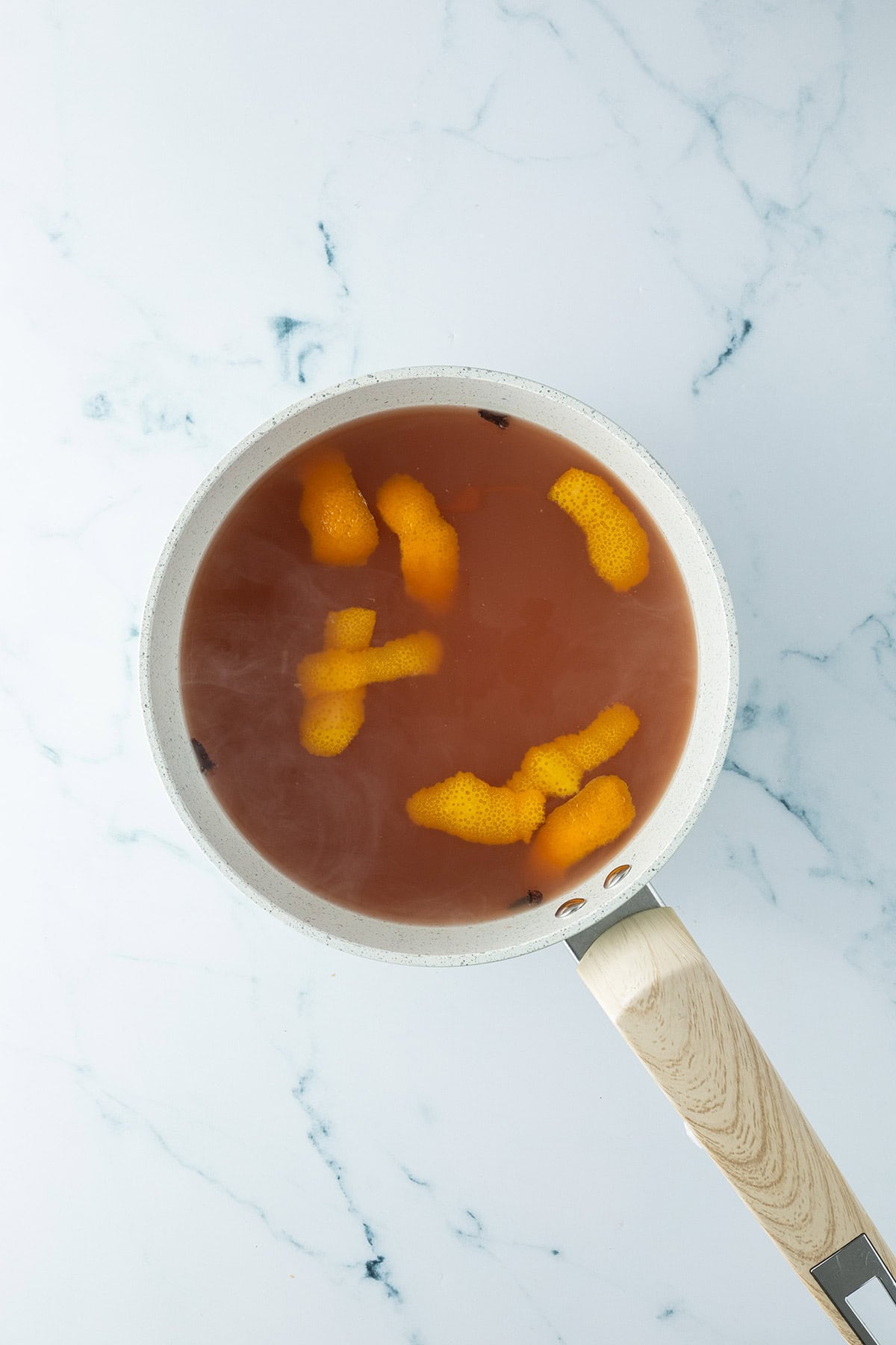 Apfelpunsch mit Orangenschale und Gew&uuml;rze in einem Topf.