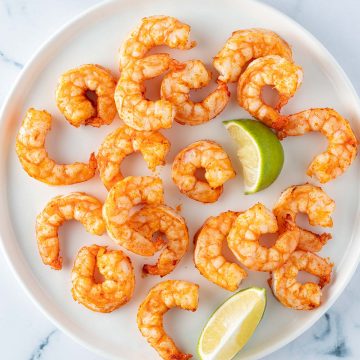 Im Airfryer zubereitete Garnelen mit Limettenspalten auf einem Teller.