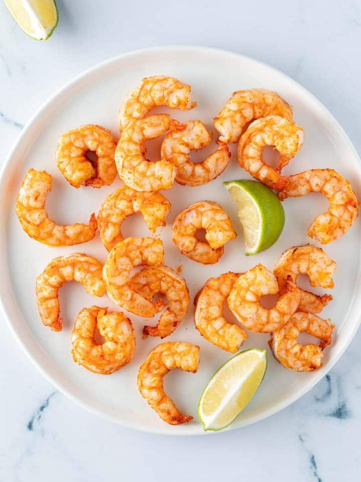 Im Airfryer zubereitete Garnelen mit Limettenspalten auf einem Teller.