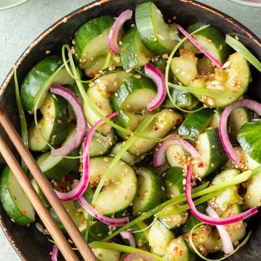 Asiatischer Gurkensalat mit Sesam&ouml;l in einer Sch&uuml;ssel, serviert mit eingelegten roten Zwiebeln und Fr&uuml;hlingszwiebeln.