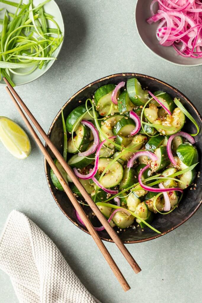 Asiatischer Gurkensalat mit Sesam&ouml;l in einer Sch&uuml;ssel, serviert mit eingelegten roten Zwiebeln und Fr&uuml;hlingszwiebeln.