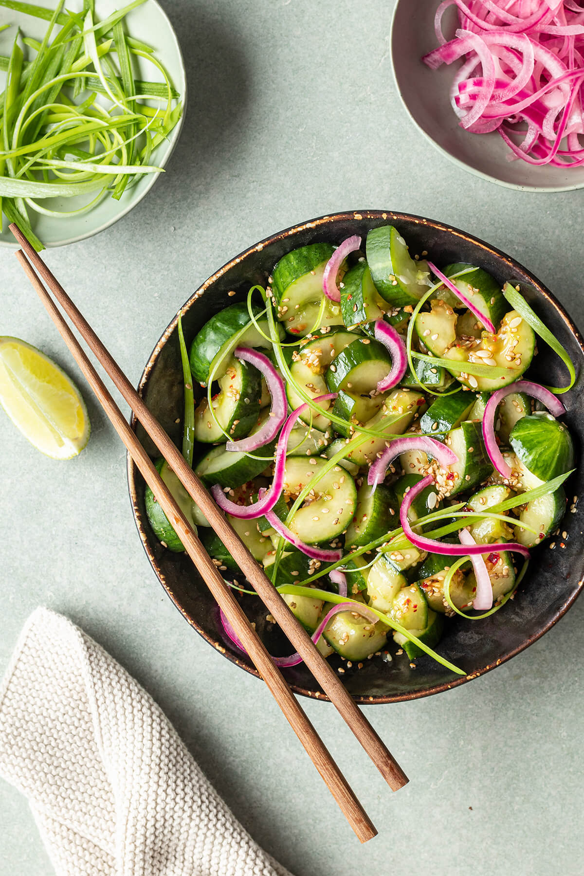 Asiatischer Gurkensalat mit Sesam&ouml;l in einer Sch&uuml;ssel, serviert mit eingelegten roten Zwiebeln und Fr&uuml;hlingszwiebeln.