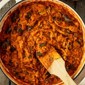 Auberginen Curry mit Linsen und Zwiebeln in einer cremigen Tomatensauce in einer gro&szlig;en Pfanne auf einem rustikalen Holzuntergrund, im Bildrand Naan.