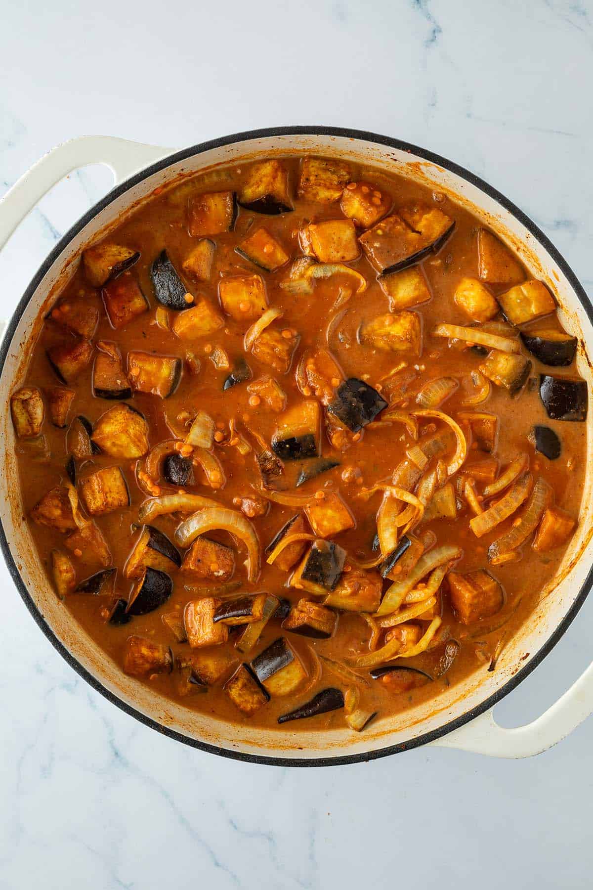 Ger&ouml;stete Auberginen-W&uuml;rfel und Zwiebelringe in einer gro&szlig;en Pfanne mit Kokosmilch, passierten Tomaten und ungekochten Linsen.