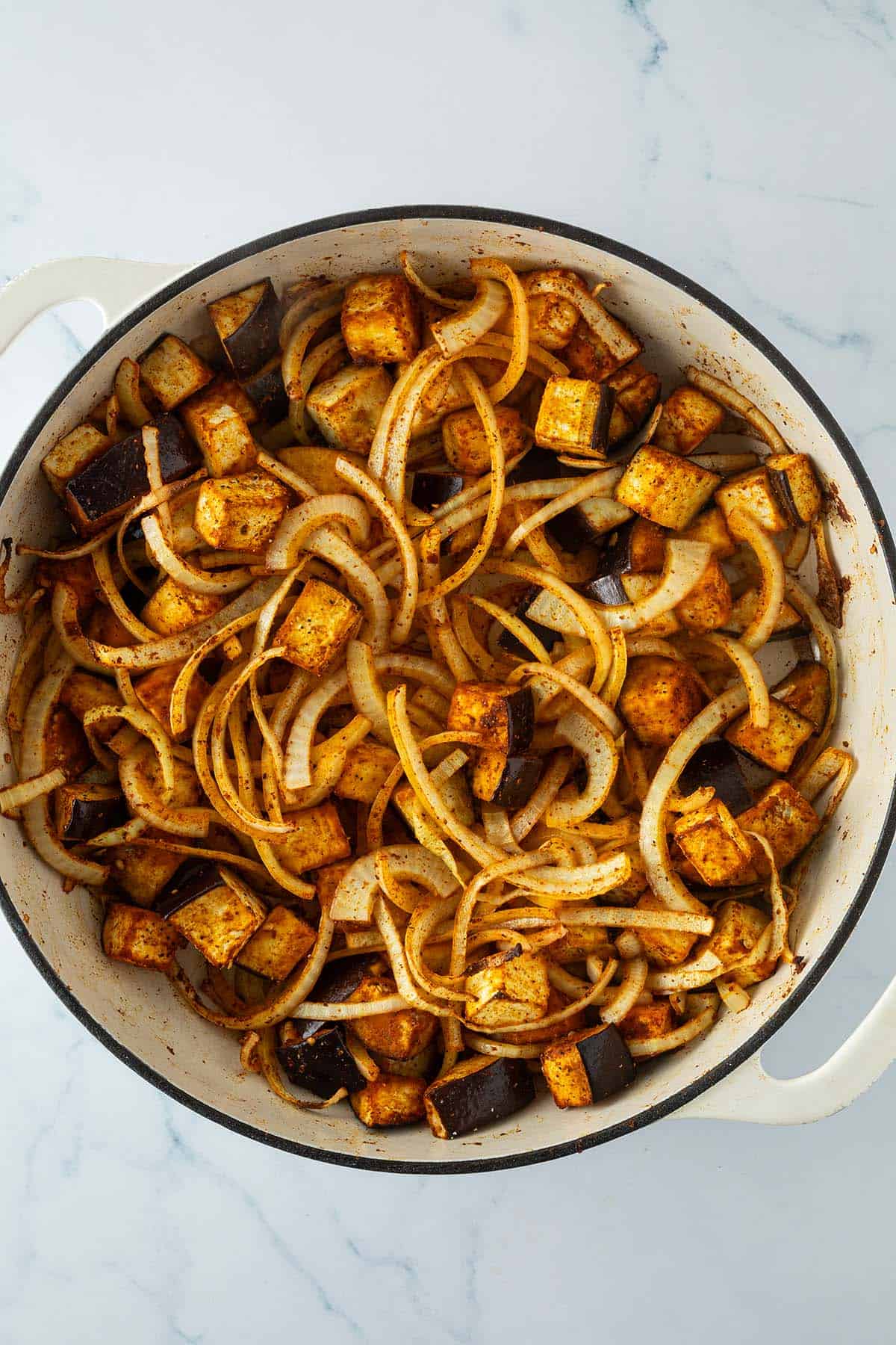Eine gro&szlig;e Pfanne mit im Ofen ger&ouml;steten Auberginen-W&uuml;rfeln und Zwiebelringen.