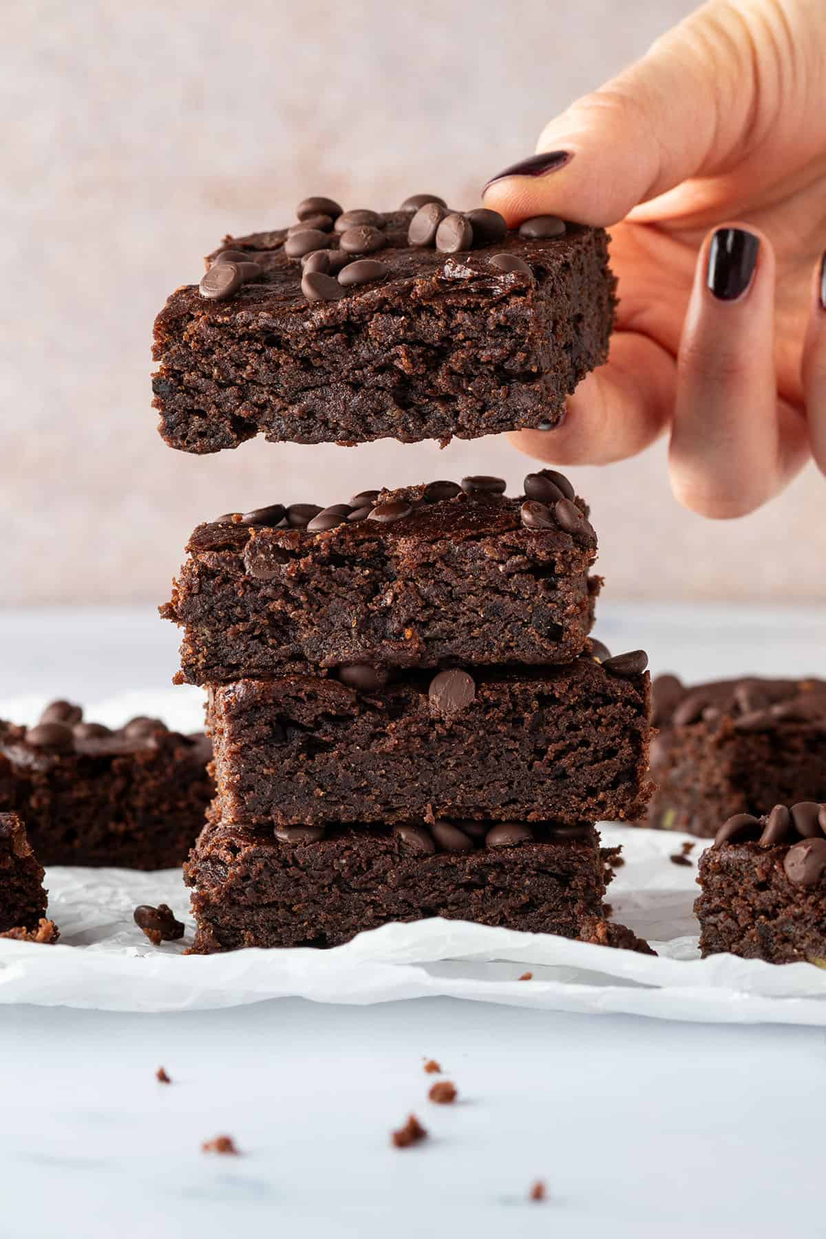 Ein Stapel an vier saftigen Brownies, wo der oberste gerade von einer Hand weggenommen wird.