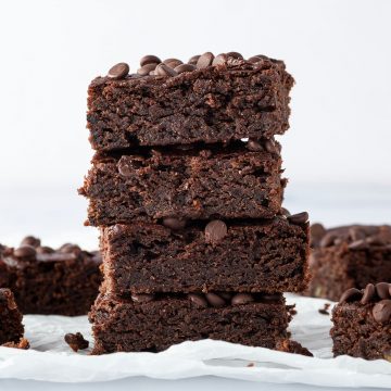 Ein Stapel aus vier saftigen Avocado Brownies, mit weiteren Brownies im Hintergrund.