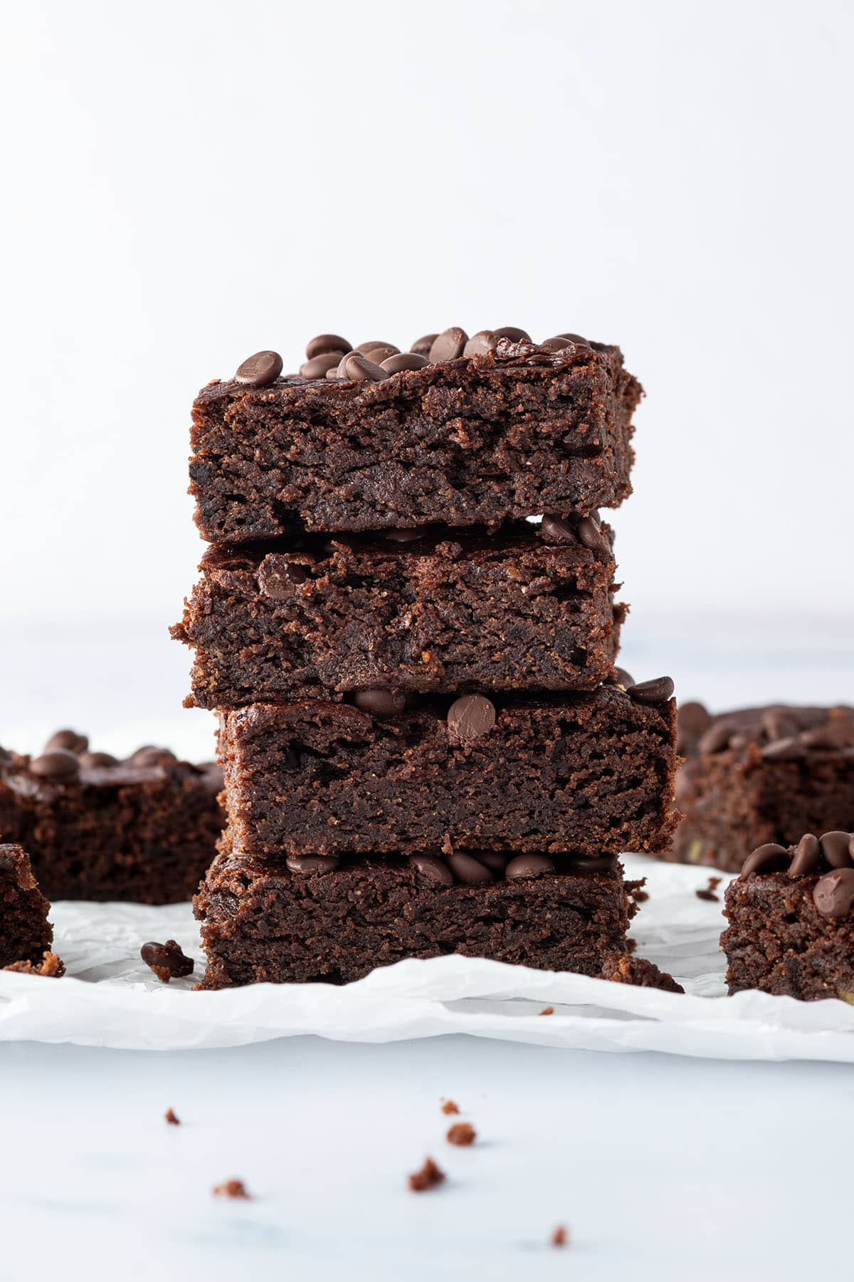 Ein Stapel aus vier saftigen Avocado Brownies, mit weiteren Brownies im Hintergrund.