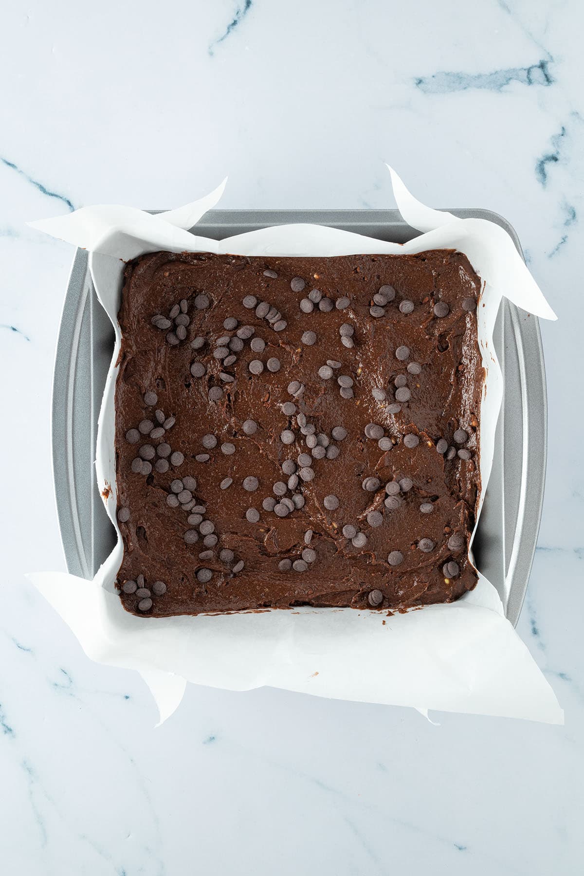 Brownie-Teig in einer viereckigen Backform, die mit Butterpapier ausgelegt wurde.